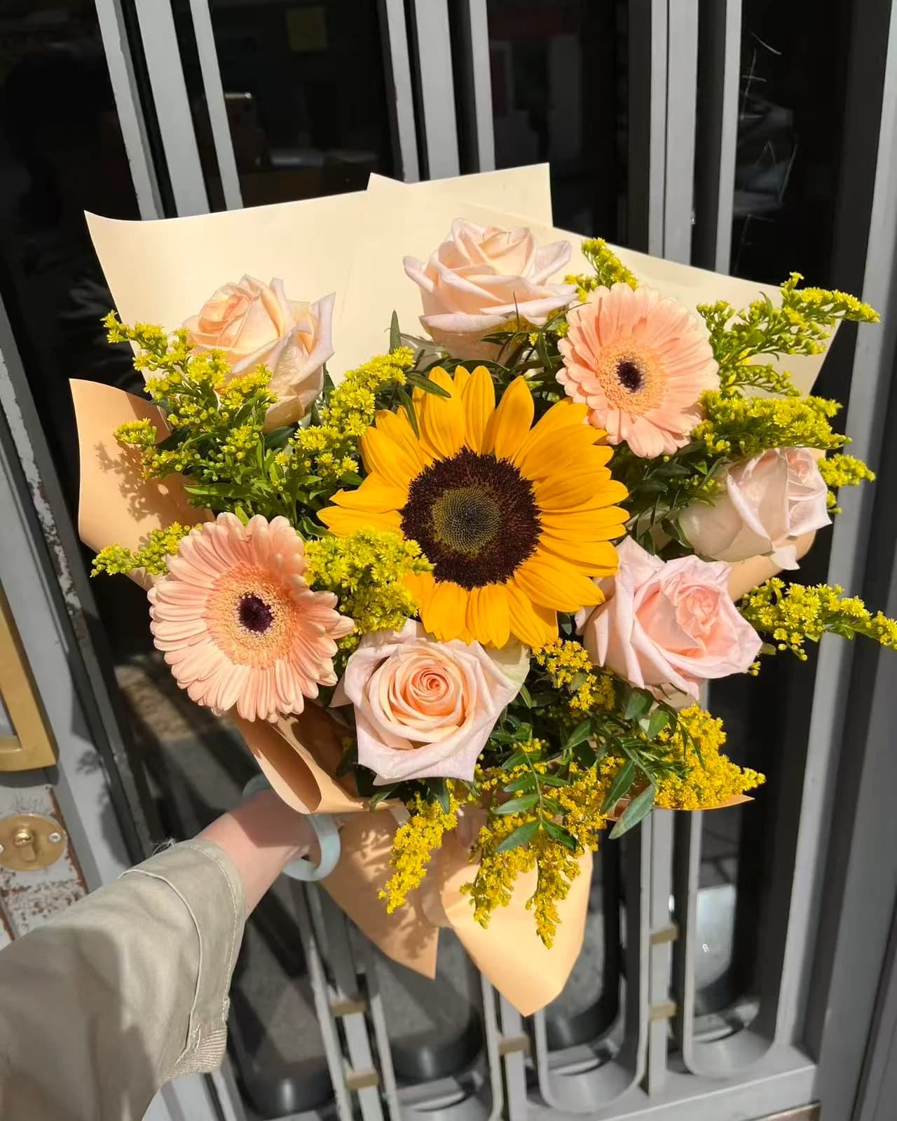 Ramo Mediodía con un girasol, rosas y gerberas melocotón y solidago en papel crema y melocotón